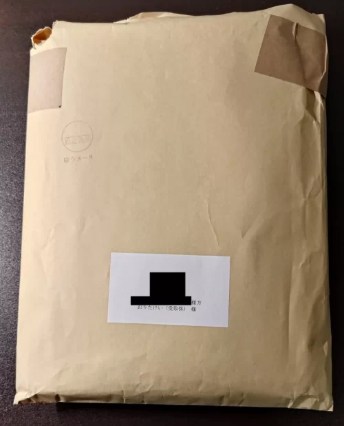 A4サイズの茶封筒。書籍が一冊入っていて少し膨らんでいる。Amazonのマーケットプレイス出品者から購入した商品で、Amazonの段ボールで配送されないことを説明している